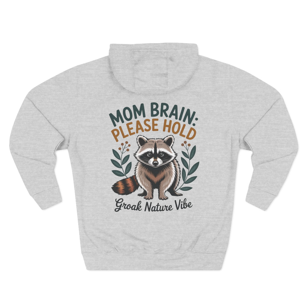 A light heather gray hoodie shown from the back, featuring a graphic of a raccoon with the text 'MOM BRAIN: PLEASE HOLD' and 'Groak Nature Vibe' in green, orange, and dark gray lettering. For mom.