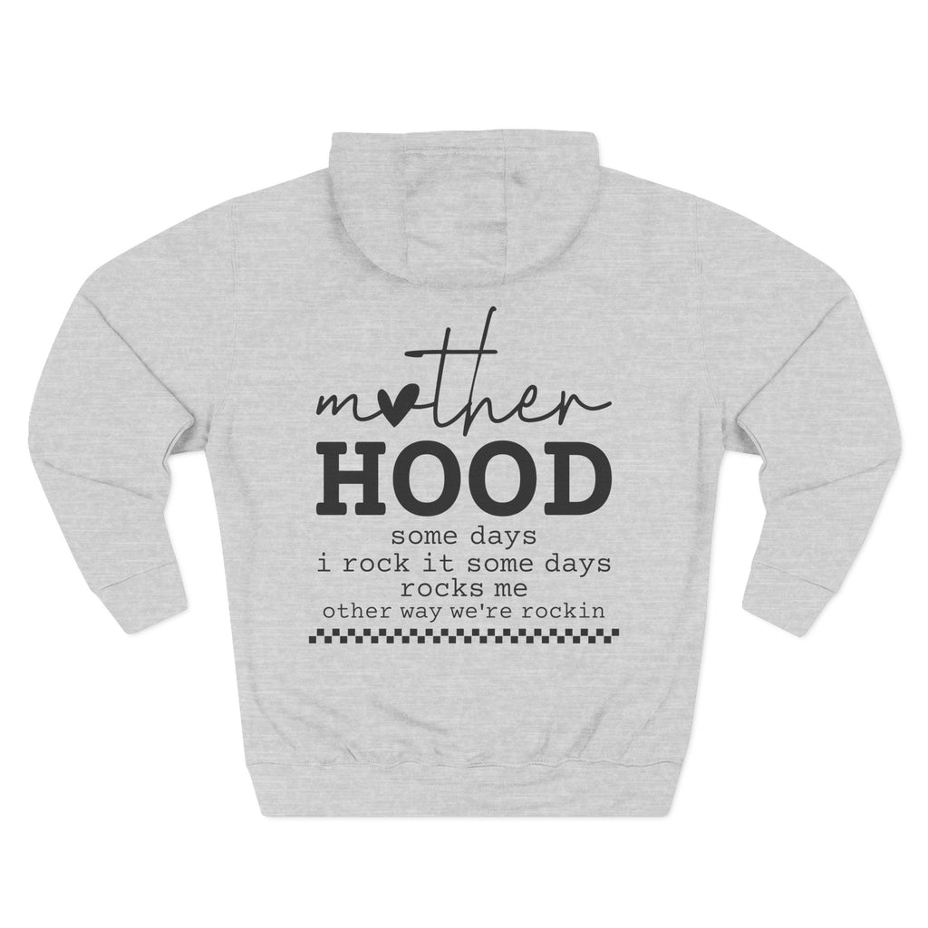 A light grey heather pullover hoodie shown from the back, featuring a black graphic print that reads 'mother HOOD' with a heart replacing the letter 'o' in 'mother', followed by the phrase 'some days i rock it some days rocks me other way we're rockin' with a small checkered line at the bottom. Special gift for mom