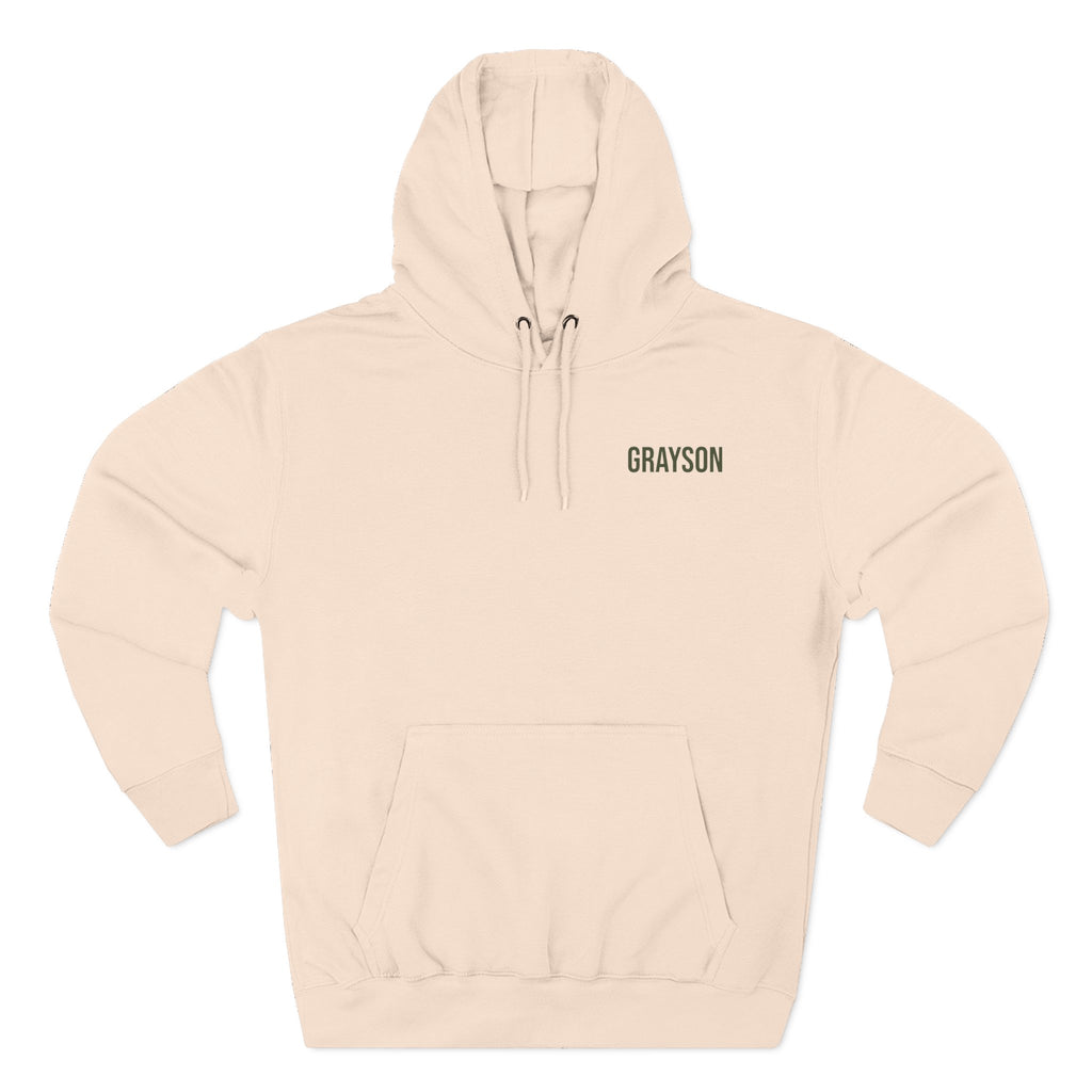 Front view of a pale pink personalizable hoodie. The front has a small black name on the chest is personalizable, and the back features a large square graphic print of a mountain landscape in muted green, yellow, and brown tones. Special gift for him, dad, grandpa, boyfriend etc.