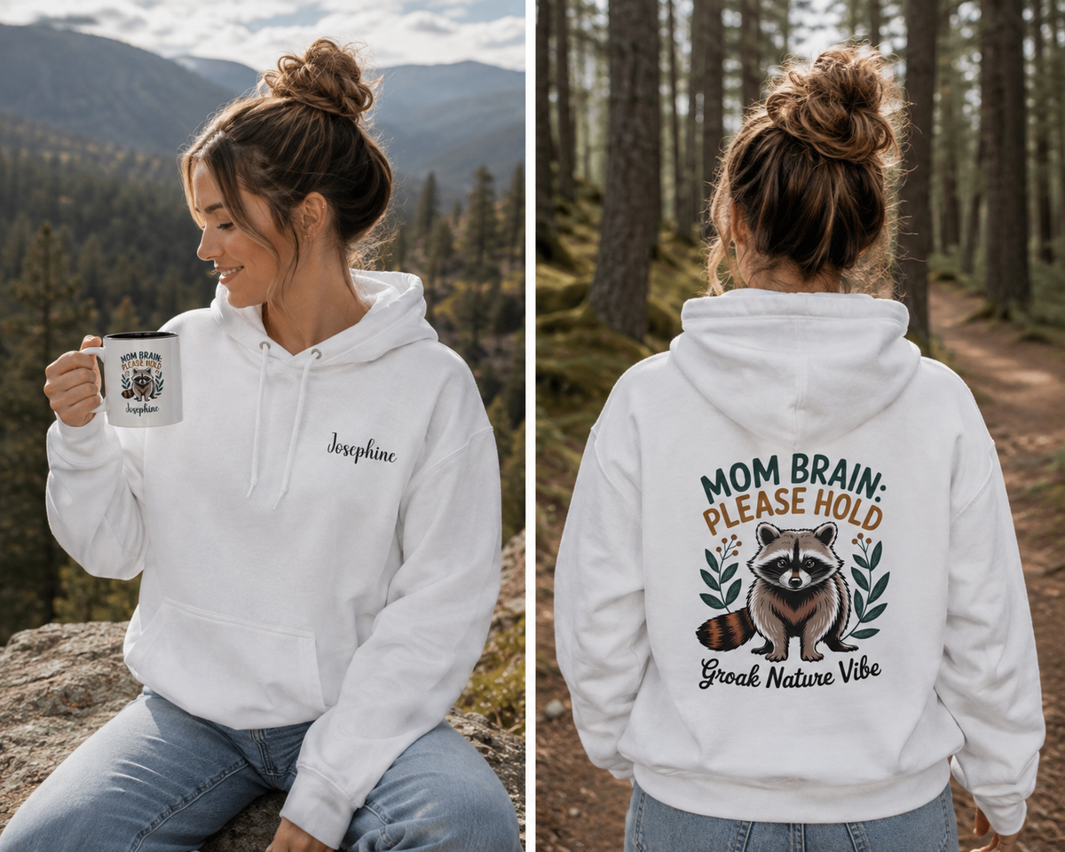 A woman wearing a white pullover hoodie is shown in a split view, seated outdoors on the left holding a mug and standing on the right facing a forest trail. The front has a small black script name on the chest, and the back has a large raccoon graphic with the text 'MOM BRAIN: PLEASE HOLD Groak Nature Vibe. For mom