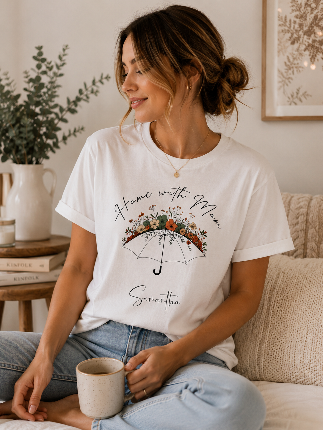 A woman sitting on a couch wearing a white graphic t-shirt with a floral umbrella design and the text 'Home with Me' and 'Samantha'.
