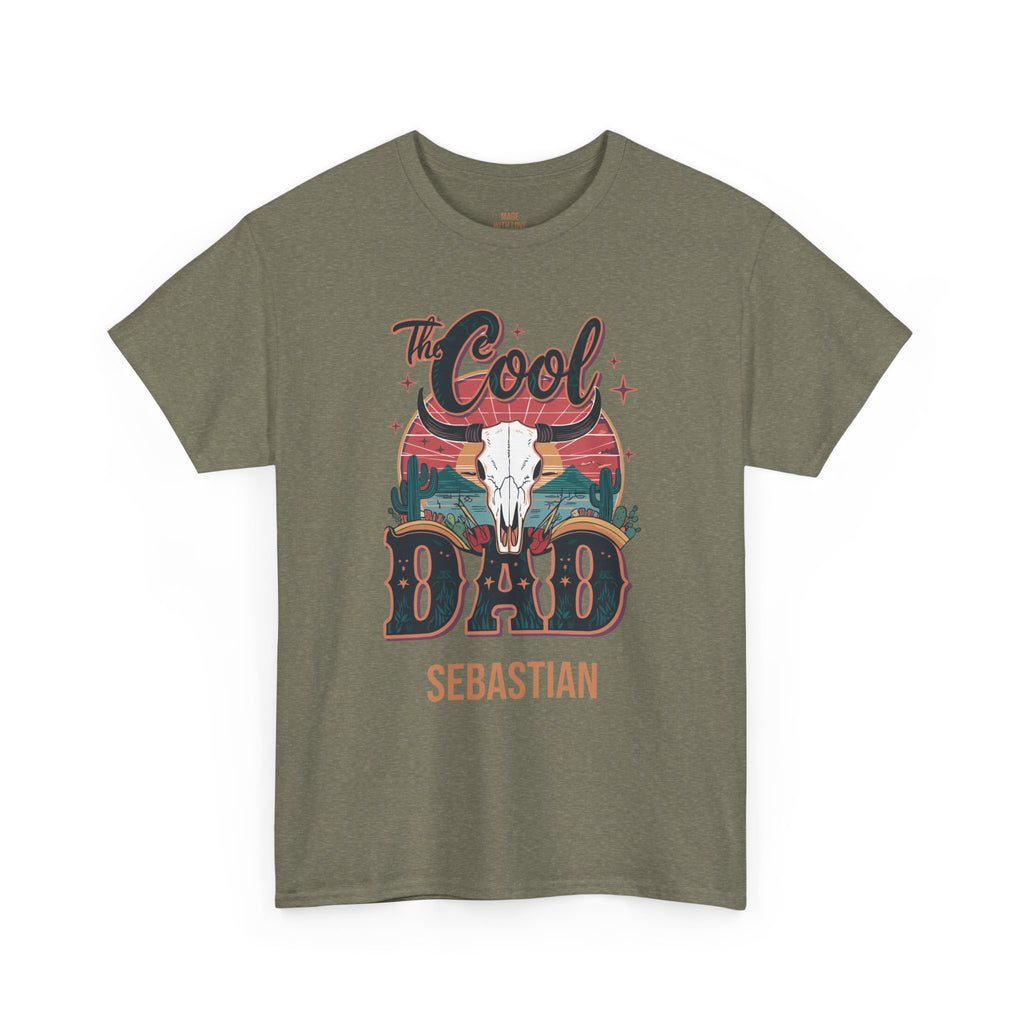 An olive green short-sleeve t-shirt with a western-themed graphic on the front. The graphic features a white bull skull, the words 'The Cool', 'DAD', and 'SEBASTIAN' in stylized lettering, and a sunset background.
