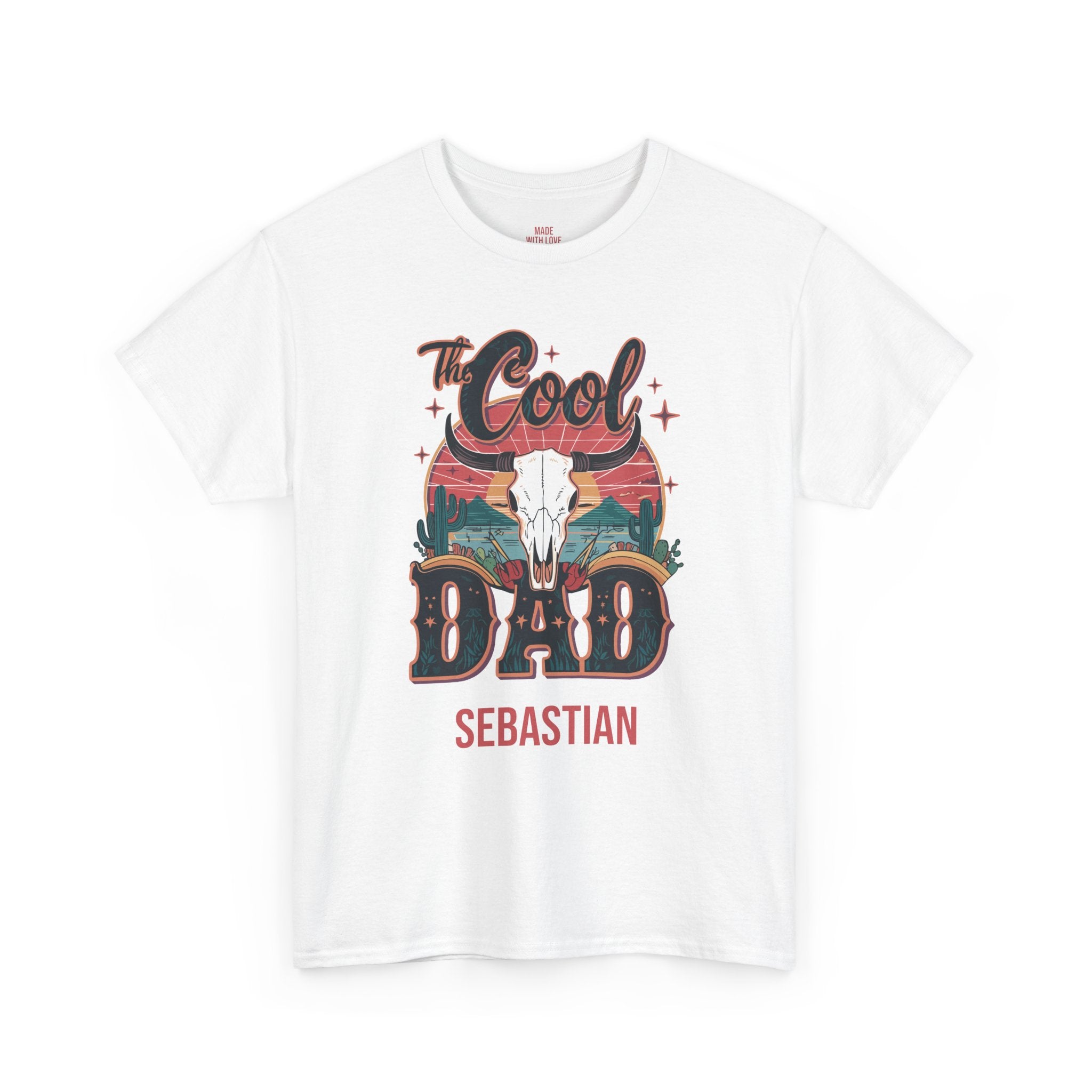 A white short-sleeve crewneck t-shirt featuring a graphic print on the front. The design includes the text 'The Cool DAD' in a western-style font, a white skull, and a sunset landscape, with 'SEBASTIAN' printed below in red.