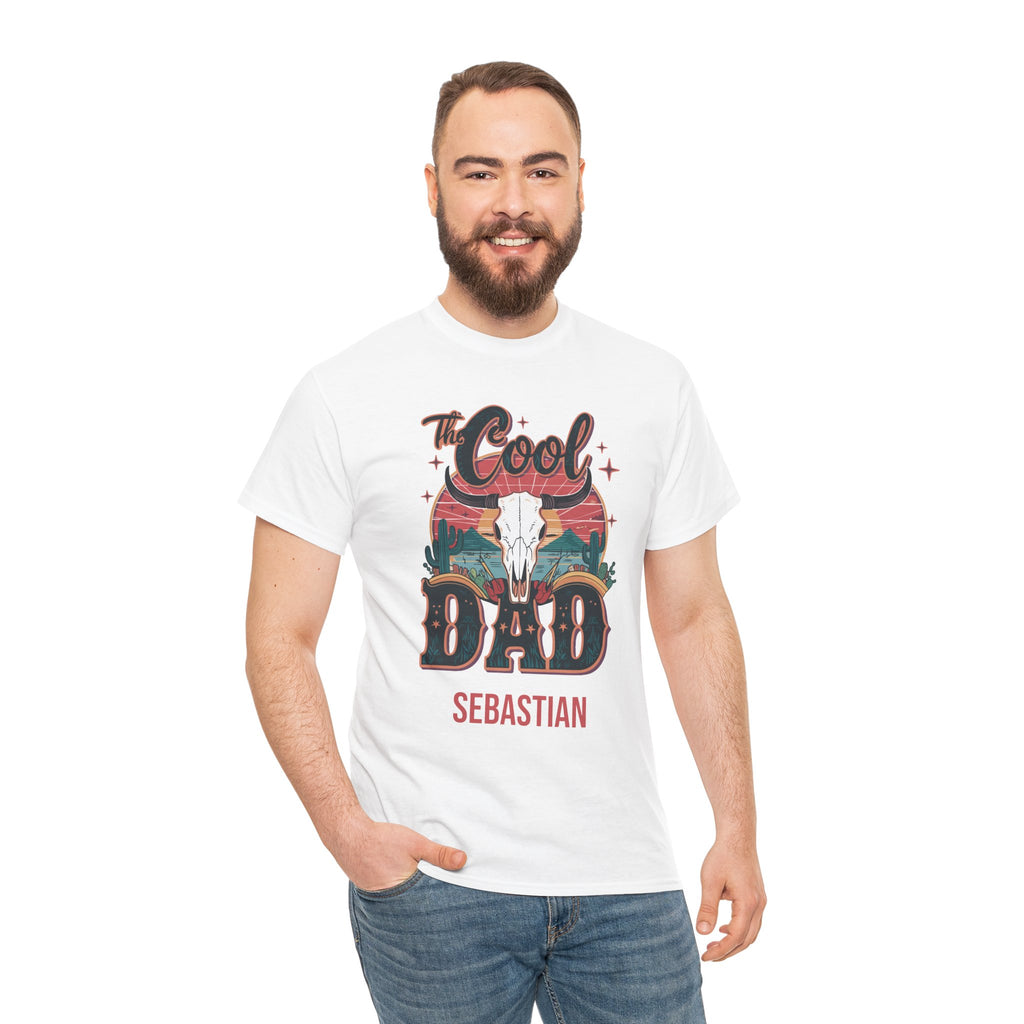 A man wearing a white graphic t-shirt with a 'The Cool Dad Sebastian' design featuring a cowboy skull and sunset landscape, paired with blue jeans, against a plain white background.