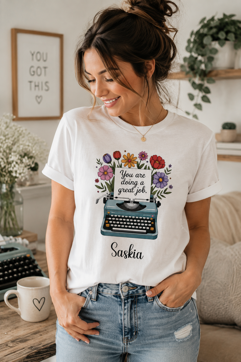 A woman wearing a white graphic t-shirt with a floral typewriter design and the text 'You are doing a great job' and 'Saskia'.